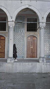 A woman leans out of a historical arched doorway at the topkapi palace in istanbul, showcasing ancient ottoman architecture.