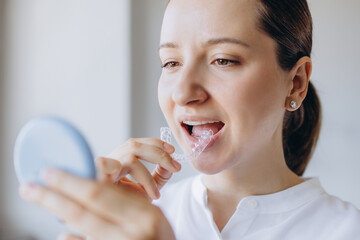 Woman Is Putting On A Transparent Aligner While Looking In A Small Mirror. Dental Health Medical Care Concept.