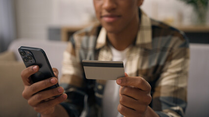 Unrecognizable African American man hold plastic bank credit card smartphone virtual money cashless finance transaction pay online internet payment banking mobile phone shopping purchase guy home buy