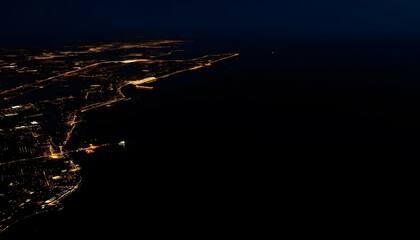 Aerial view of a coastal city at night, with a winding road and scattered lights illuminating the landscape against a dark background