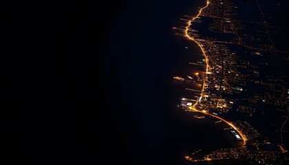 Obraz premium Aerial view of a coastal city at night, with a winding road and scattered lights illuminating the landscape against a dark background