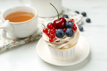 Tasty cupcake with different berries and tea on white marble table, closeup