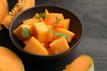 Pieces of ripe Cantaloupe melon in bowl on dark wooden table, closeup