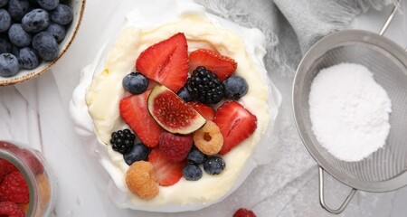 Pavlova cake (meringue dessert) with whipped cream, fresh berries, fig and powdered sugar on table, top view