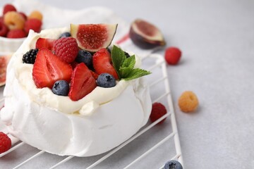 Pavlova cake (meringue dessert) with whipped cream, fresh berries, mint and fig on light grey table, closeup