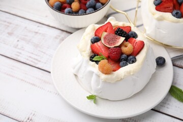 Pavlova cake (meringue dessert) with whipped cream, fresh berries, fig and mint on white wooden table, closeup