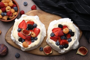 Pavlova cake (meringue dessert) with whipped cream, fresh berries and fig on brown table, flat lay