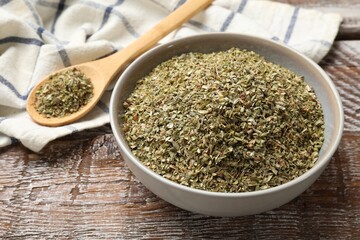 Dried oregano in bowl and spoon on wooden table, closeup