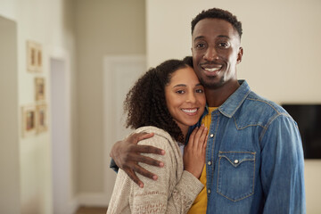 Smiling young multiracial couple standing arm in arm at home