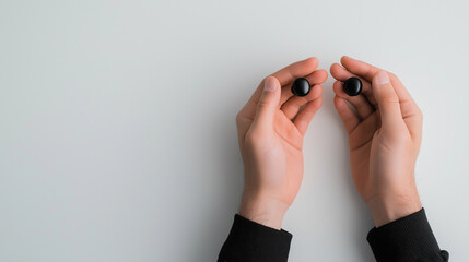 Fototapeta premium Two hands holding a pair of wireless earbuds, ready for use, isolated on a white background.