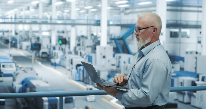 Portrait of a Handsome Middle Aged Engineer with Glasses Using Laptop Computer and Looking Around a Factory Facility with Equipment Producing Modern Electronic Components for Different Industries