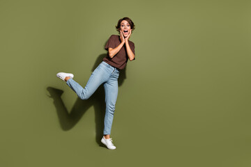 Full length photo of overjoyed astonished girl wear oversize t-shirt denim pants palms on cheek staring isolated on green color background
