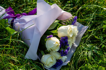 A bouquet of white roses with the addition of purple Limonium sinuatum flowers lies on the grass