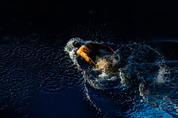 Female athlete swims with a butterfly style. Splashes of water scatter in different directions
