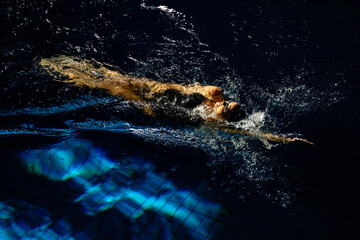 Female athlete swims with a back stroke. Splashes of water scatter in different directions