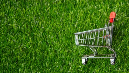 A miniature shopping cart on vibrant green grass with copy space symbolizes sustainable shopping....