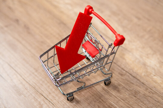 A miniature shopping cart with downward-pointing red arrow. Retail trends, decrease in sales, sales drop concept.