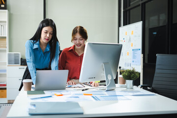 Business documents on office table with smart phone, tablet and laptop computer and graph with social network diagram and two colleagues discussing data in office.