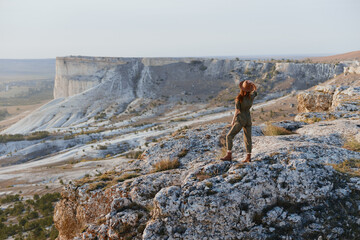 Fototapeta premium Woman standing on cliff edge with outstretched arms in front of her embracing the beauty of nature and adventure