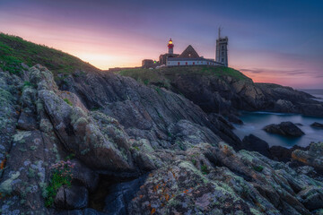 Saint-Mathieu Lighthouse at sunrise, with cliff rocks on foreground, on Pointe Saint-Mathieu in...