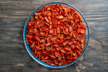 Sun dried red tomato in a glass bowl on wooden table , closeup, top view