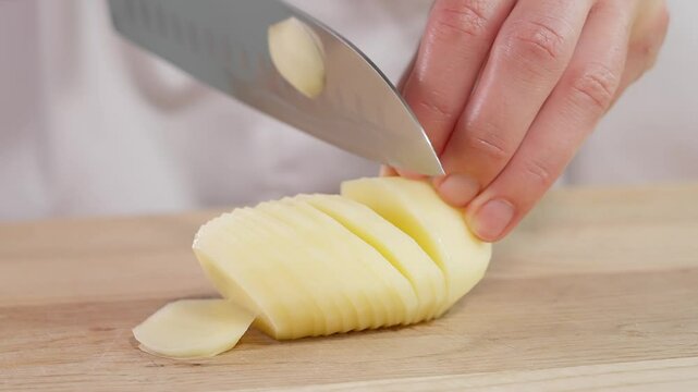 Macro. Girl cuts potatoes into thin slices with a sharp knife, on a wooden board. Boiled potatoes, potato dishes. Front view, close-up