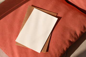 Blank paper card mockup, crafted envelope on terracotta red textured pillow background with natural...