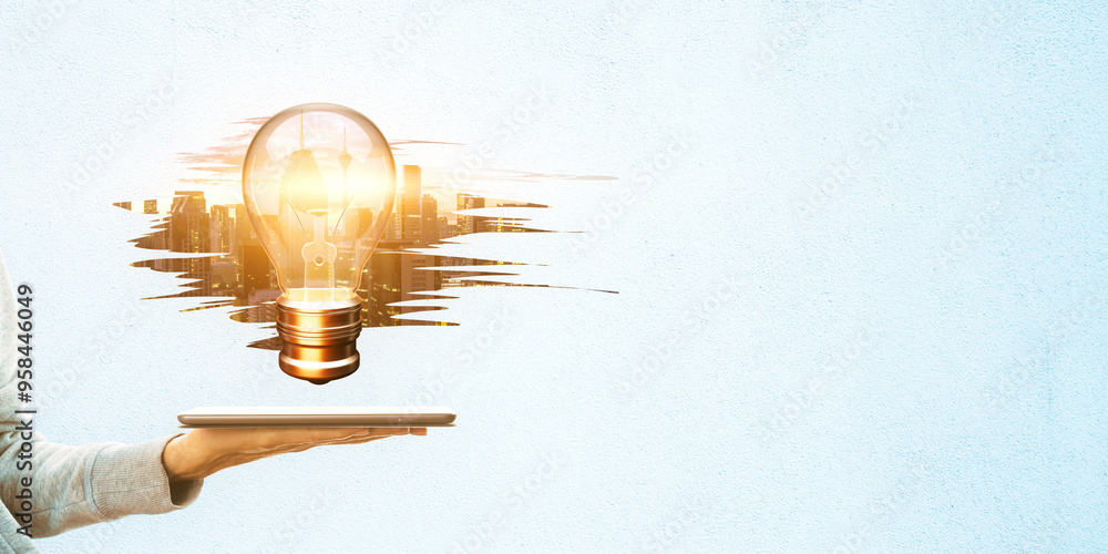 Poster close up of female hand holding tablet with glowing light bulb on abstract weathered city on light b
