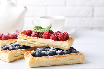 Tasty puff pastries with berries on white wooden table, closeup