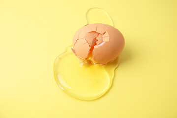 Broken raw egg with shell on yellow background
