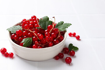 Fresh red currants and leaves in bowl on white table, closeup. Space for text