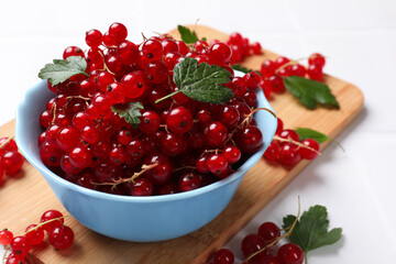 Fresh red currants in bowl and green leaves on white table, closeup