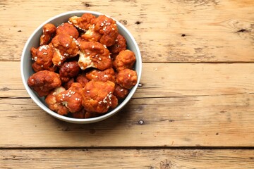Tasty cauliflower buffalo wings in bowl on wooden table, top view. Space for text