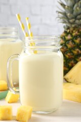 Tasty pineapple smoothie in mason jar and fresh fruit on white wooden table