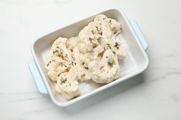 Uncooked cauliflower steaks with spices in baking dish on white marble table, top view