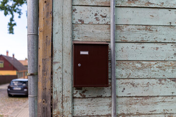 A brown mailbox attached to the weathered wood wall of a quaint house in a quiet neighborhood during the daytime
