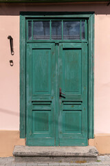 A charming green double door on a pastel pink building's facade in a quaint village setting