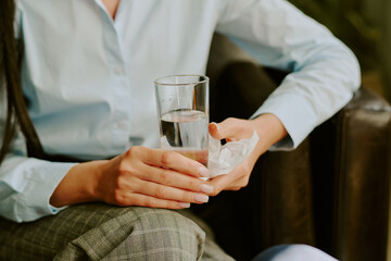Close-up of a person holding a glass of water and a napkin while sitting on a sofa in relaxed posture