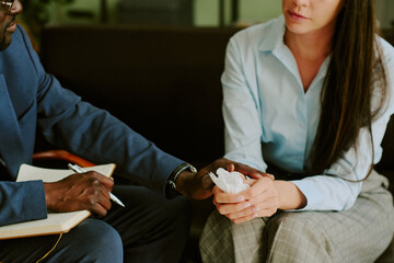 Professional holding notepad engaging in counseling session with client holding tissue, discussing...