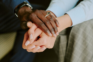 Close-up of hands of interracial couple with wedding rings, symbolizing unity and love, against...