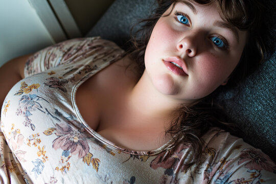curvy woman lies on a couch in a floral top her fuller figure relaxed and her expression soft and naturally beautiful