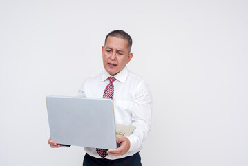 A middle aged asian manager standing looking puzzled while reading a laptop held in his arms. Isolated on a white background.