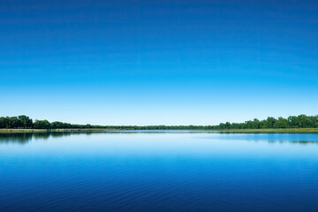 A tranquil lake mirroring a clear blue sky on a warm summer day. The gentle ripples on the water create a sense of peace and serenity.