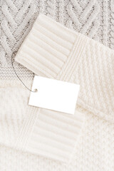 Fototapeta premium Top view of warm woven casual comfortable sweater or cardigan knitted from soft white wool or merino yarn with sleeves and price tag or label with information about price discount on black friday sale