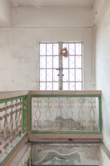 A weathered staircase railing leads to a vintage window, illuminating the aged interior with soft...