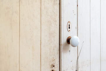 A close-up of a vintage door knob on a rustic white wooden door, highlighting its design and character in a serene setting.