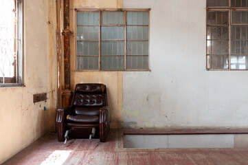 A vintage armchair in an empty room with rustic walls and natural light streaming through tall...