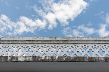Elegant architectural detail of a decorative wall against a bright blue sky adorned with fluffy white clouds.