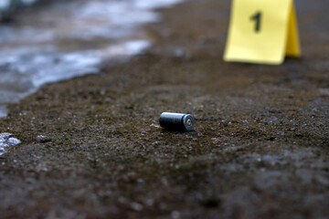 Evidence regarding firearms, Pistol bullet shell on cement floor with blurred number one on yellow...