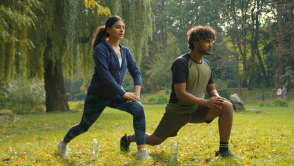 Confident determined Indian couple Arabian man woman girl guy doing lunges squats exercises sport morning workout in park outdoors fit friends people team sports body weight training personal coach